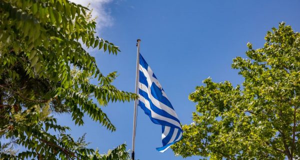 greek-flag-waving-against-blue-sky-background-7ZVUWAS