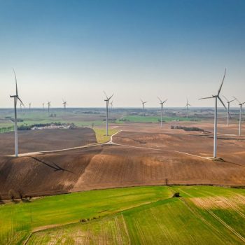 aerial-view-of-wind-turbines-on-green-field-sunny-2023-11-27-04-52-23-utc